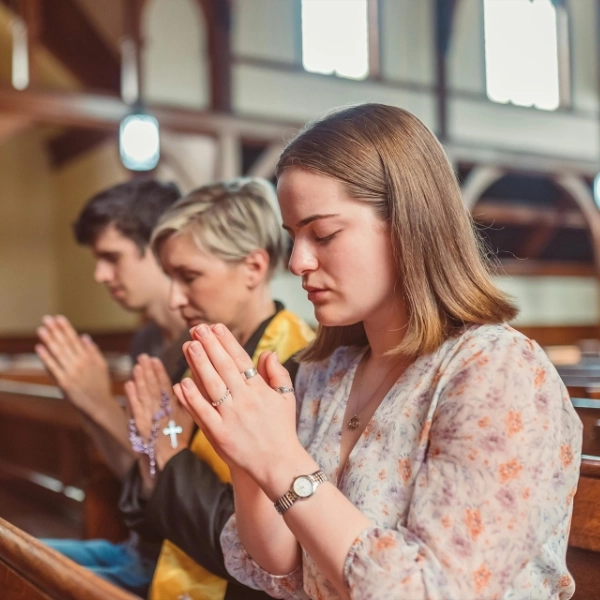 Tres personas oran con las manos unidas y los ojos cerrados dentro de una iglesia durante un retiro espiritual.