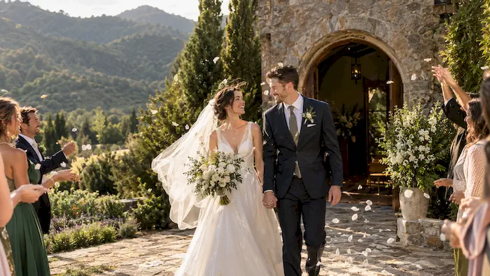 Newlywed couple leaving a chapel surrounded by gardens and mountains on their way to the wedding reception
