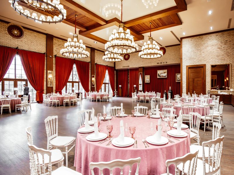 restaurant hall with round tables white napoleon chairs red curtains brick walls and chandeliers
