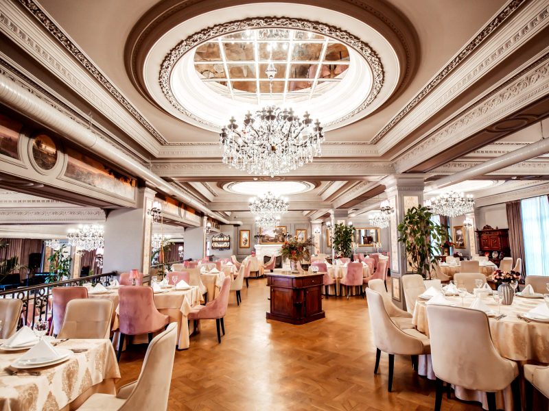 restaurant hall with round and square tables some chairs and plants