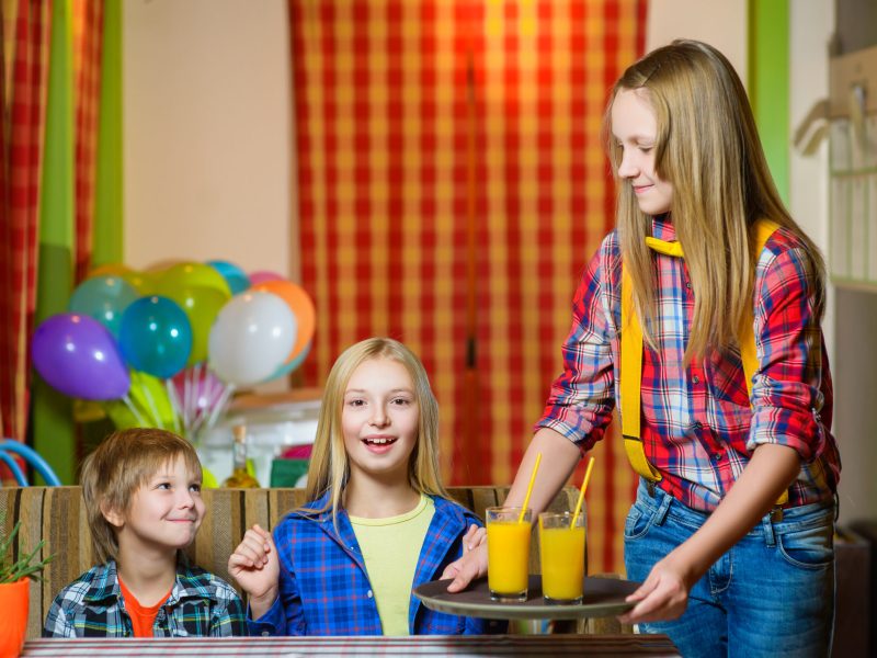 Happy cute smiling girl waiter holding a tray with juice.
